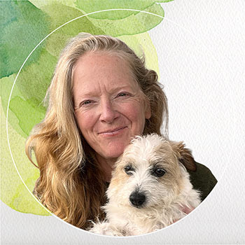 A woman with long hair. She's smiling and holding a small shaggy dog.